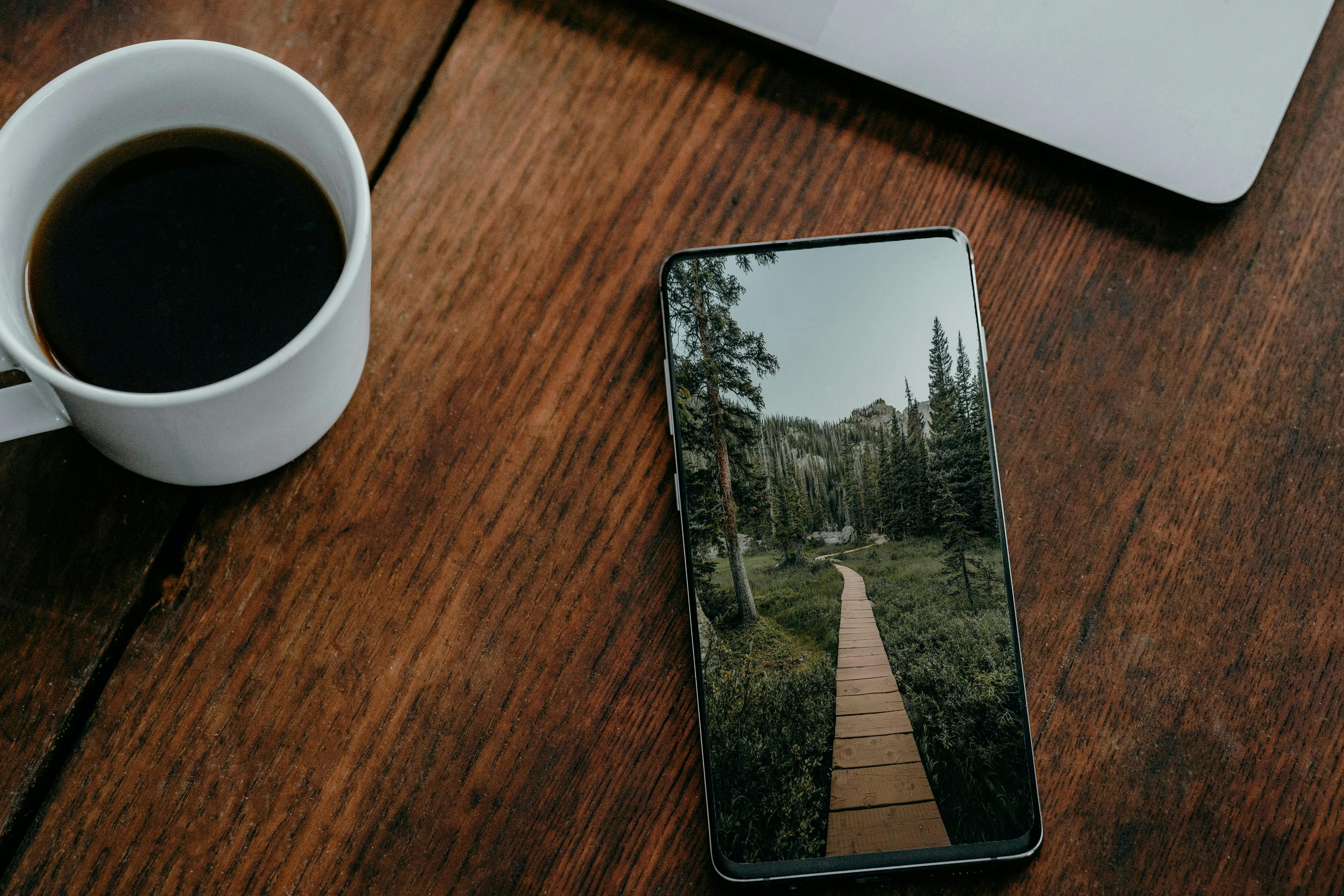 a cell phone sitting on top of a wooden table next to a cup of coffee