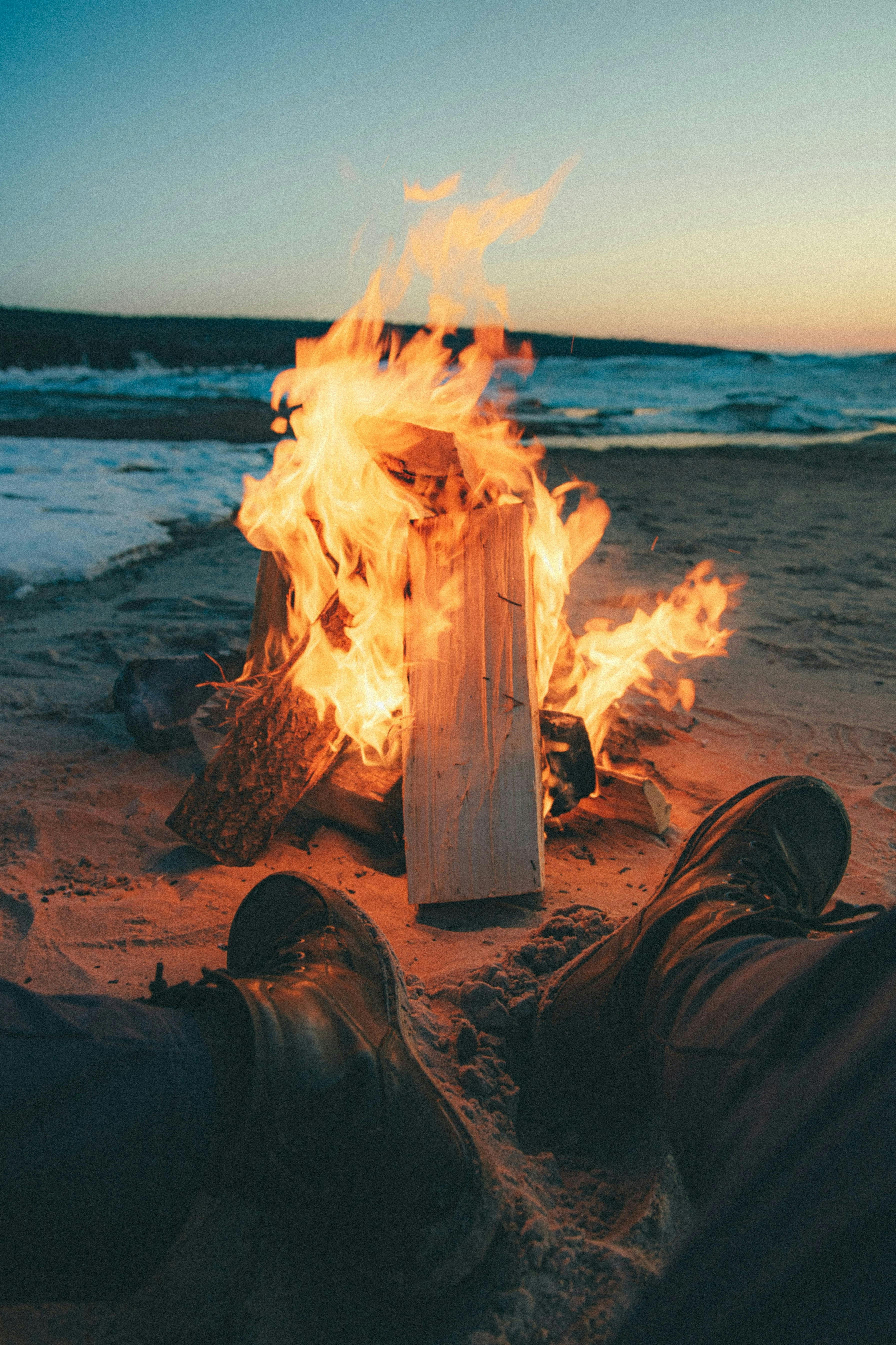 a person sitting in front of a fire on the beach