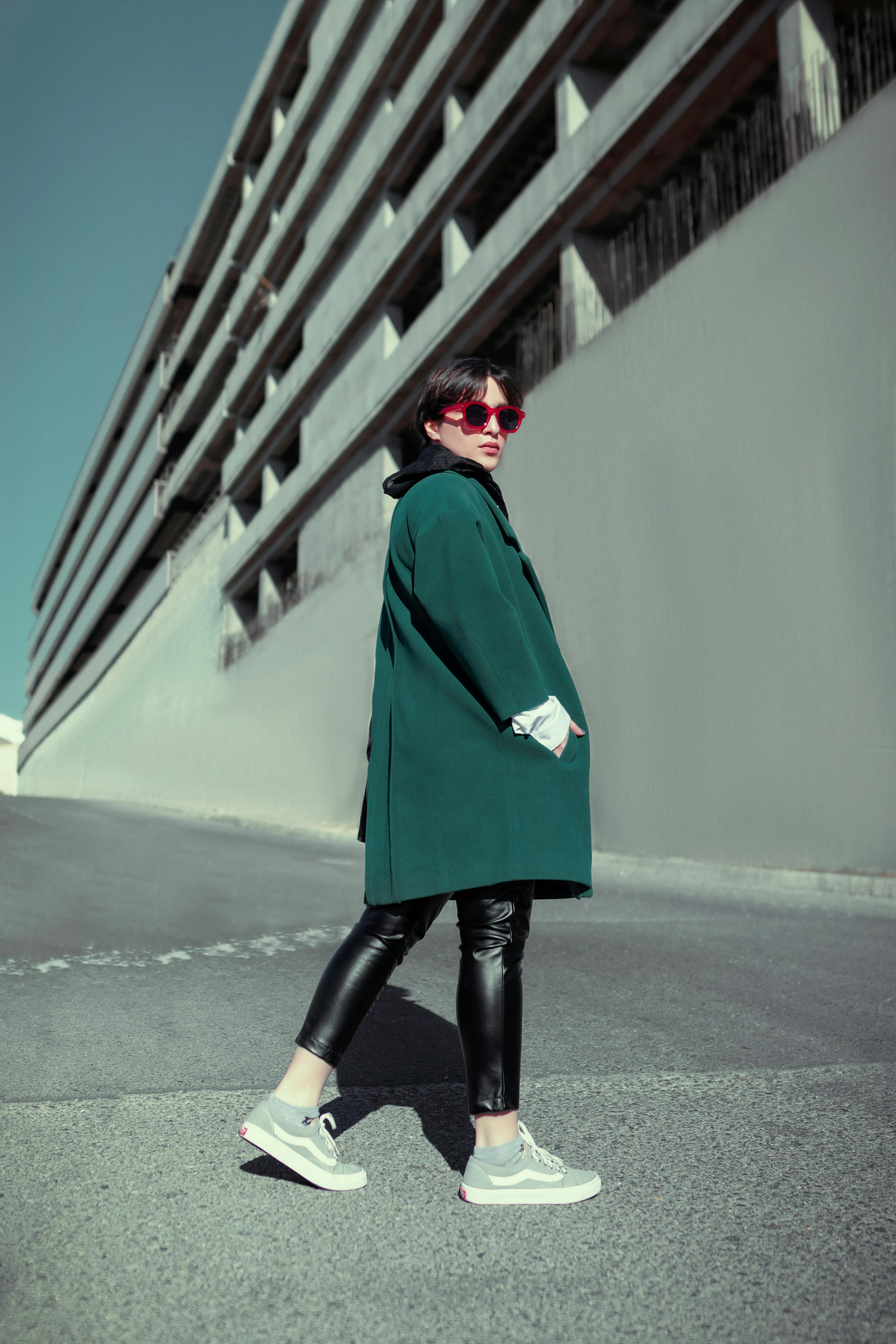a person in a green coat and sunglasses standing in front of a building