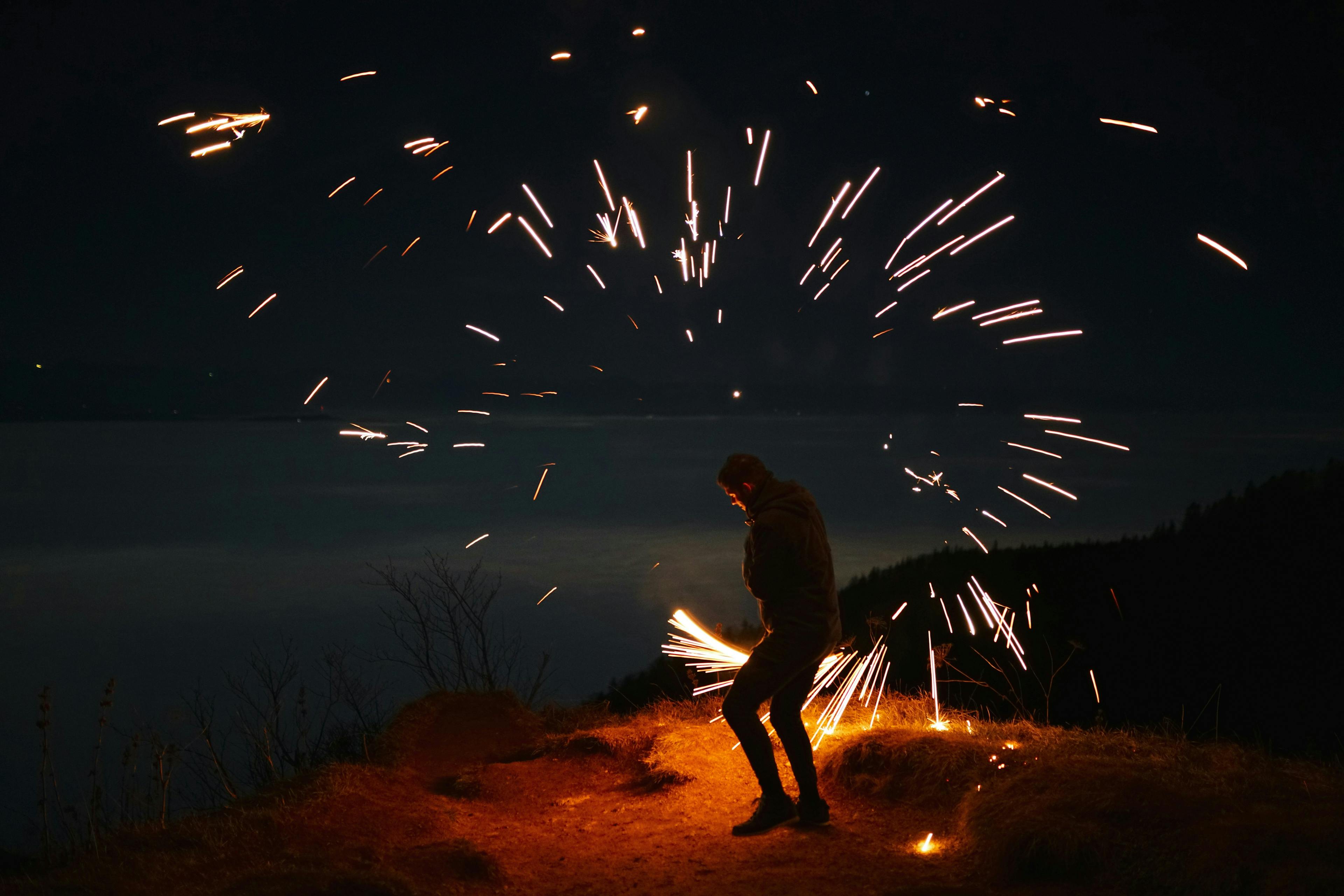 a man standing on a hill with fireworks in the sky
